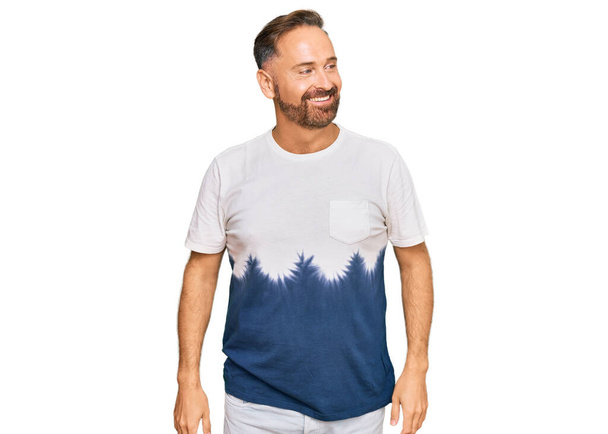 Hombre guapo de mediana edad que usa una camiseta casual de teñido de corbata mirando hacia un lado con sonrisa en la cara, expresión natural. riendo confiado.  - Foto, imagen