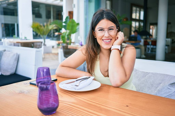 若い美しいヒスパニック系の女性が幸せな笑顔。レストランでカメラを見てテーブルの上に座って - 写真・画像