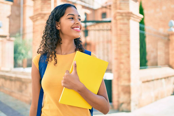 Молода афроамериканська студентка посміхається з книжки в університетському містечку.. - Фото, зображення