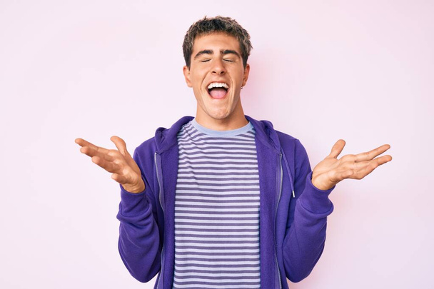 Молодий красивий чоловік в повсякденному фіолетовому светрі святкує божевілля і божевілля за успіх з піднятими руками і закритими очима кричить схвильовано. концепція переможця
  - Фото, зображення