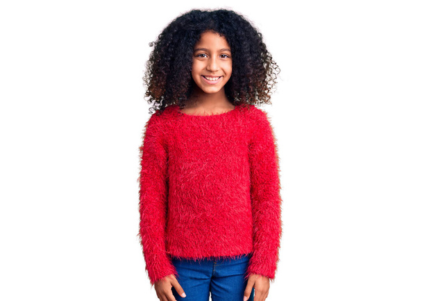 Enfant afro-américain aux cheveux bouclés portant un pull d'hiver décontracté à l'air positif et heureux debout et souriant avec un sourire confiant montrant les dents  - Photo, image