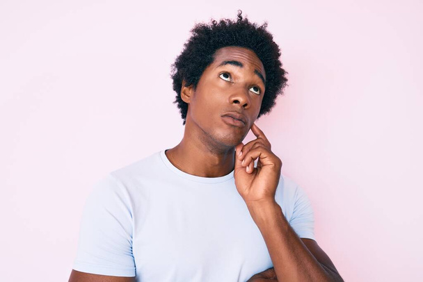 Jóképű afro-amerikai férfi afro haj visel alkalmi ruhák komoly arc gondolkodás kérdés kézzel az állán, átgondolt zavaros ötlet  - Fotó, kép