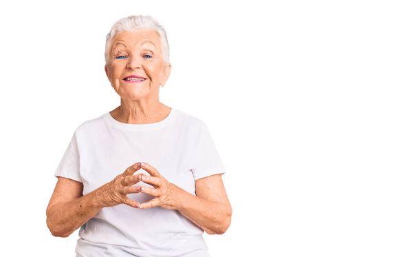 Senior gyönyörű nő kék szemekkel és ősz haj visel alkalmi fehér póló kéz együtt és ujjak keresztbe mosolyogva nyugodt és vidám. siker és optimizmus  - Fotó, kép