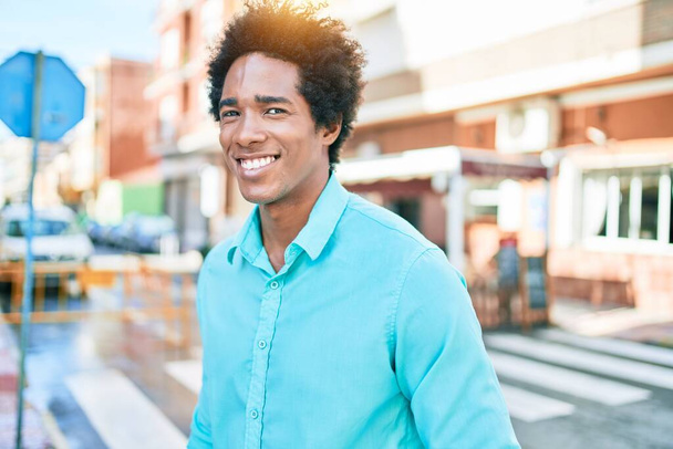 Genç, yakışıklı, Afro-Amerikan bir adam günlük giysiler giyip mutlu gülümsüyor. Yüzünde gülümsemeyle kasaba caddesinde yürürken. - Fotoğraf, Görsel