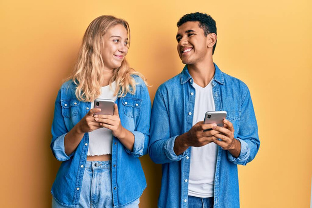 Молода міжрасова пара використовує смартфон посміхаючись дивиться в бік і дивиться на мислення
.  - Фото, зображення