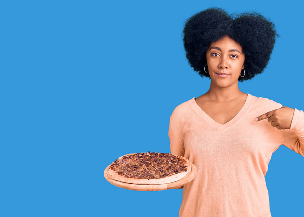 Genç Afro-Amerikan kızı İtalyan pizzasını tutarak mutlu ve gururlu bir gülümsemeyi işaret ediyor.  - Fotoğraf, Görsel