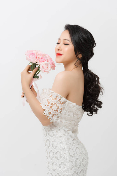 Cheerful young Asian lady wearing white dress and holding flower bouquet over white background. - Photo, Image