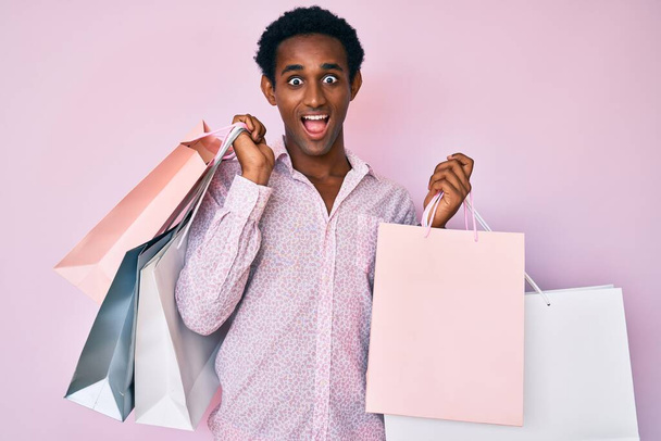Afričan pohledný muž drží nákupní tašky slaví blázen a ohromen pro úspěch s otevřenýma očima křičí vzrušený.  - Fotografie, Obrázek