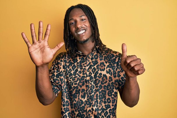 Afrikanischer Mann mit Zöpfen im Leoparden-Animal-Print-Hemd zeigt und zeigt mit Finger Nummer sechs nach oben, während er selbstbewusst und glücklich lächelt.  - Foto, Bild