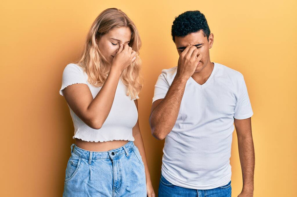 Young interracial couple wearing casual white tshirt tired rubbing nose and eyes feeling fatigue and headache. stress and frustration concept.  - Foto, afbeelding