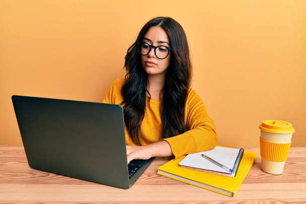 Mooie brunette jonge vrouw werken op het kantoor het dragen van bril denken houding en sobere uitdrukking op zoek zelfvertrouwen  - Foto, afbeelding