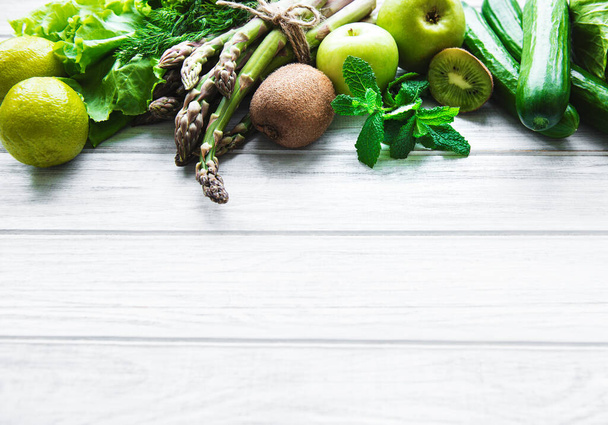 Υγιή χορτοφαγικά τροφίμων έννοια φόντο, φρέσκα πράσινα τρόφιμα επιλογή για αποτοξίνωση διατροφή, μήλο, αγγούρι, σπαράγγια, αβοκάντο, ασβέστη, σαλάτα πάνω άποψη σε ένα λευκό ξύλινο φόντο - Φωτογραφία, εικόνα