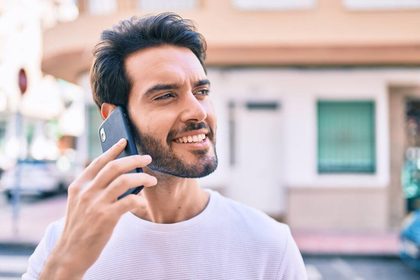 Young hispanic man smiling happy talking on the smartphone at city. - 写真・画像