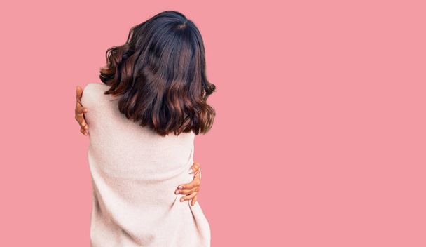 Jonge mooie gemengde ras vrouw dragen winter coltrui knuffelen zichzelf blij en positief van achteren. zelfliefde en zelfzorg  - Foto, afbeelding