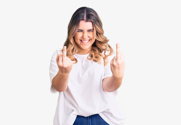 junge kaukasische Frau in lässiger Kleidung, die den Mittelfinger zeigt, wie sie dich fickt, schlechte Miene, Provokation und unhöfliche Haltung. Kreischen erregt  - Foto, Bild