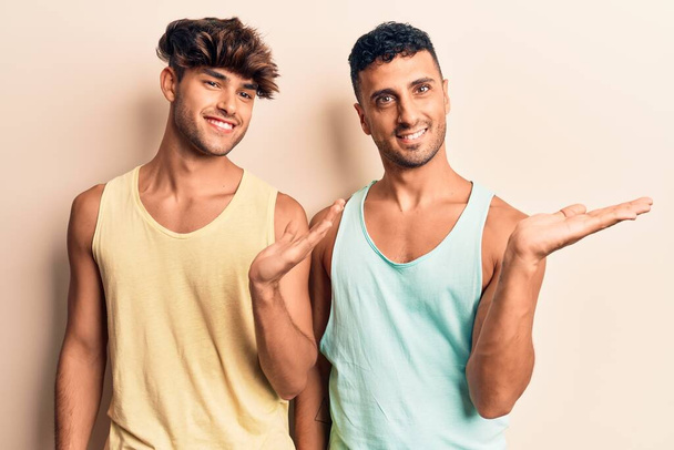 Mladý gayové pár na sobě ležérní oblečení usměvavý veselý prezentaci a ukazuje s dlaní ruky při pohledu do kamery.  - Fotografie, Obrázek