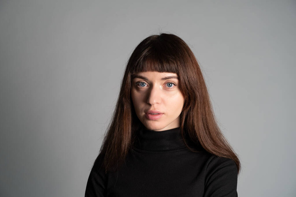 Detail studio portrét hezké brunetky, na sobě složený černý polo-neck svetr, při pohledu na kameru, na prosté šedé pozadí - Fotografie, Obrázek