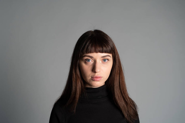 Close up studio portrait of a pretty brunette woman, wearing folded black polo-neck sweater, looking at camera, against a plain grey background - Photo, Image