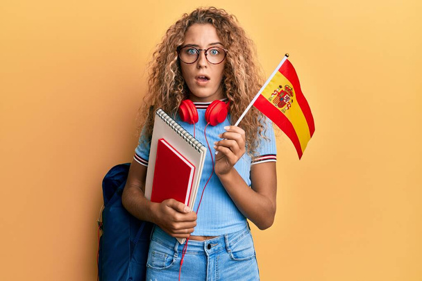 Güzel beyaz kız değişim öğrencisi İspanyol bayrağını elinde tutuyor, şüpheci ve alaycı görünüyor, ağzı açık kalmış.  - Fotoğraf, Görsel