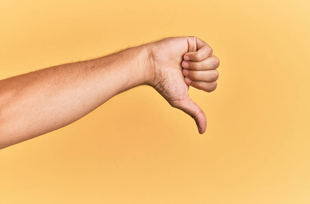 Braço e mão do homem caucasiano sobre fundo amarelo isolado fazendo polegares para baixo gesto de rejeição, desaprovação antipatia e sinal negativo  - Foto, Imagem
