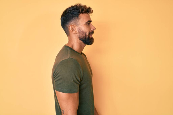 Jonge Spaanse man draagt casual kleding op zoek naar kant, ontspannen profiel poseren met een natuurlijk gezicht met zelfverzekerde glimlach.  - Foto, afbeelding