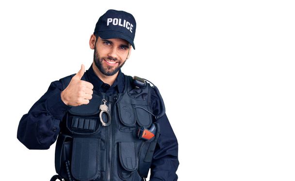Ein junger gutaussehender Mann mit Bart in Polizeiuniform macht eine glückliche Daumen-hoch-Geste mit der Hand. Zustimmender Blick in die Kamera zeigt Erfolg.  - Foto, Bild
