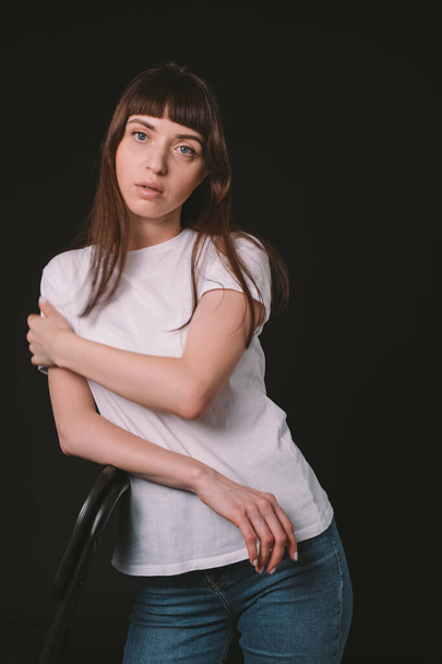 Studio portrait of a pretty brunette woman in a white blank t-shirt, against a plain black background, looking at camera - 写真・画像