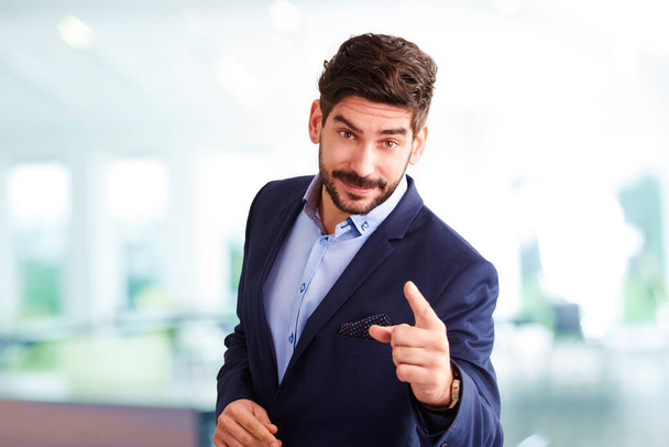 Studio portrait of young businessman points his finger at you while standing at isolated white background and looking at camera.  - Foto, Imagen