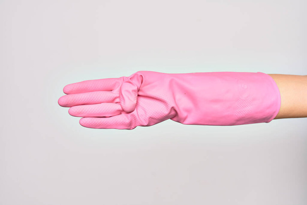 Hand of caucasian young woman wearing pink cleaning glove. Showing fingers doing number four over isolated white background - Фото, зображення