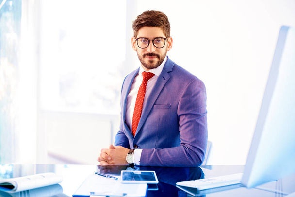 Shot of handsome businessman wearing suit and eyewear while sitting at office desk and working on his computer.  - Foto, Bild