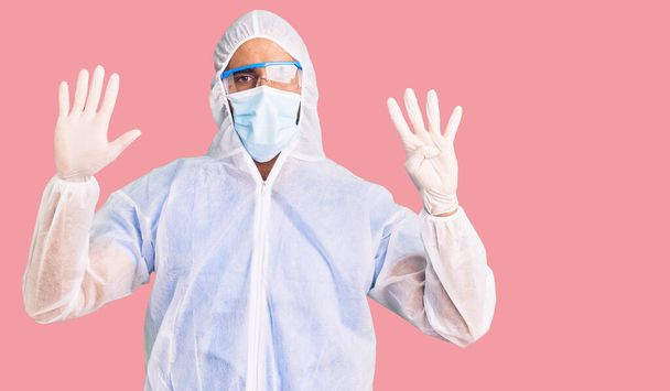 Jonge Latijns-Amerikaanse man draagt doktersbescherming coronavirus uniform en medisch masker tonen en wijzen met vingers nummer negen, terwijl hij vol vertrouwen en gelukkig lacht.  - Foto, afbeelding