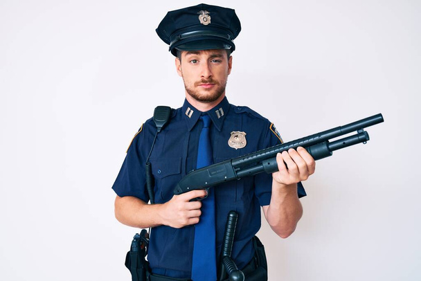 Молодий кавказький чоловік у поліцейській формі тримає рушницю скептично і нервово, розчаровуючись через проблеми. негативна людина
.  - Фото, зображення
