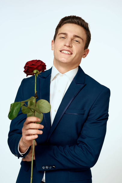 A man in a suit with a rose in his hands a gift date light background - Zdjęcie, obraz