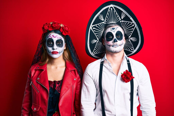 Couple wearing day of the dead costume over red with serious expression on face. simple and natural looking at the camera.  - Photo, Image