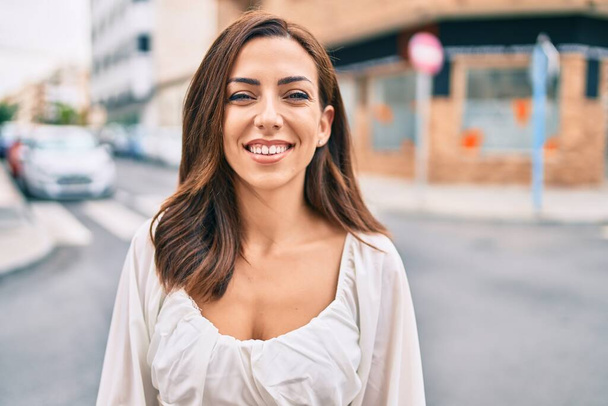Νεαρή Ισπανίδα γυναίκα χαμογελά ευτυχισμένη περπατώντας στην πόλη. - Φωτογραφία, εικόνα