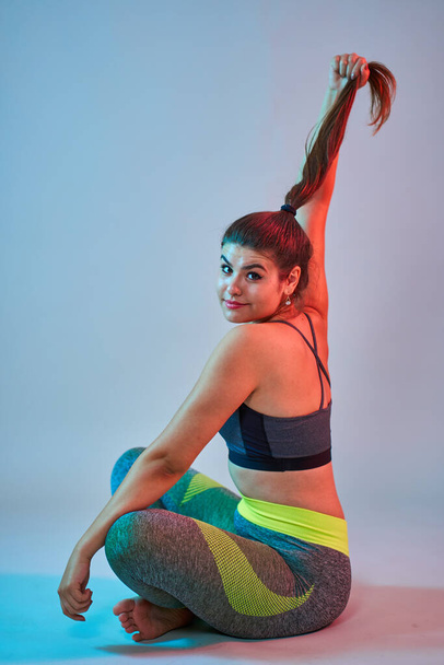 Plus size confident beautiful young woman doing fitness exercises, blue-red toning, studio shot - Fotó, kép