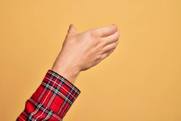 Valkoihoisen nuorukaisen käsi näyttää sormiaan eristetyn keltaisen taustan päällä pitäen näkymätöntä esinettä, tyhjä käsi leikaten ja tarttuen eleeseen. - Valokuva, kuva