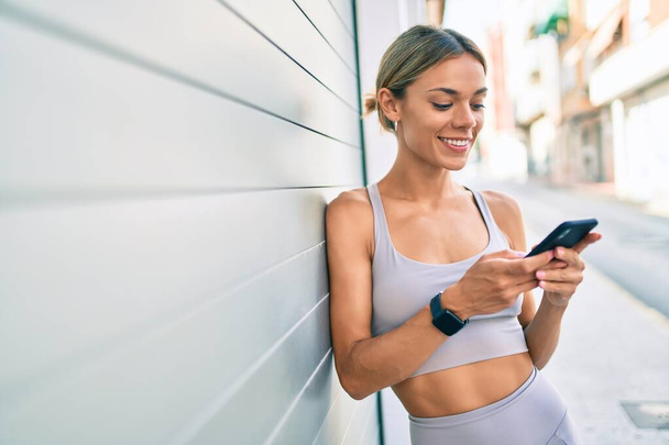 Genç Kafkas fitness kadını spor kıyafetleri giyiyor açık havada akıllı telefon kullanıyor. - Fotoğraf, Görsel