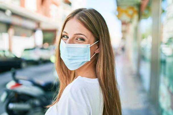 Young caucasian woman wearing coronavirus protection medical mask walking at the city - Valokuva, kuva
