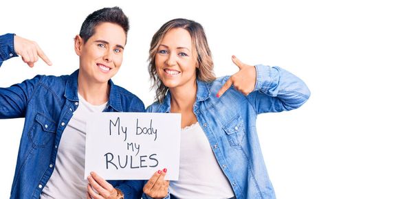 Un paio di donne tenendo il mio corpo le mie regole striscione puntando il dito verso un sé sorridente felice e orgoglioso  - Foto, immagini