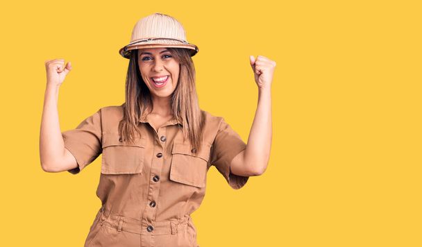 Young beautiful woman wearing explorer hat screaming proud, celebrating victory and success very excited with raised arms  - Foto, afbeelding
