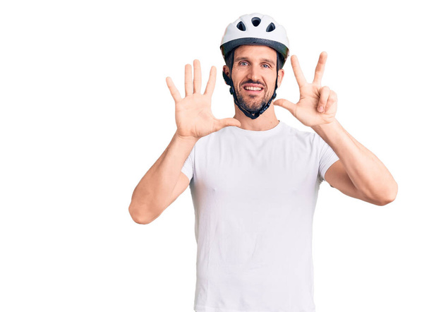 Bisiklet kaskı takan yakışıklı genç adam 8 numarayı gösterip işaret ederken kendinden emin ve mutlu bir şekilde gülümsüyor..  - Fotoğraf, Görsel