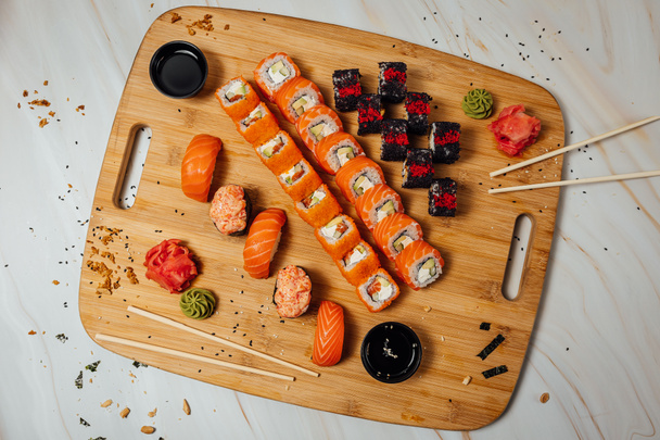 板の上には生姜やわさび、チョップスティックなどの寿司ロール、テーブルの上には寿司ロールが置かれている。  - 写真・画像