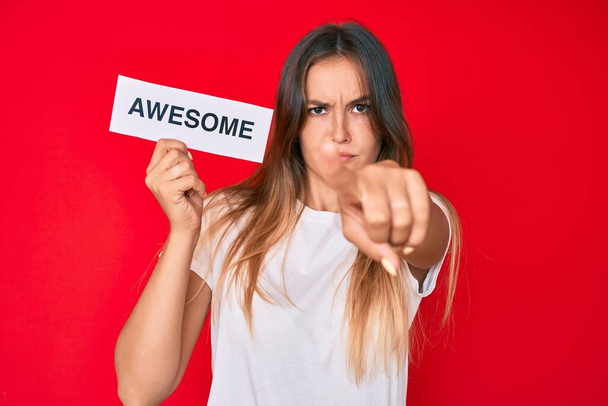 Beautiful caucasian woman holding awesome banner pointing with finger to the camera and to you, confident gesture looking serious  - Фото, изображение