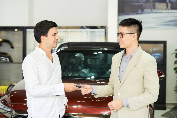 Nuori liikemies seisoo auton showroom ja saada avain uuden auton Aasian myyntimies - Valokuva, kuva