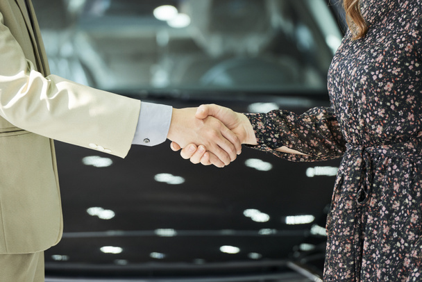 Крупним планом чоловік і жінка стоять і струшують руки один одному після угоди в автосалоні
 - Фото, зображення