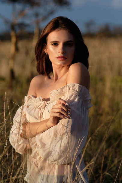 a girl in a white blouse and black skirt stands in a yellow field in the setting sun - Foto, imagen