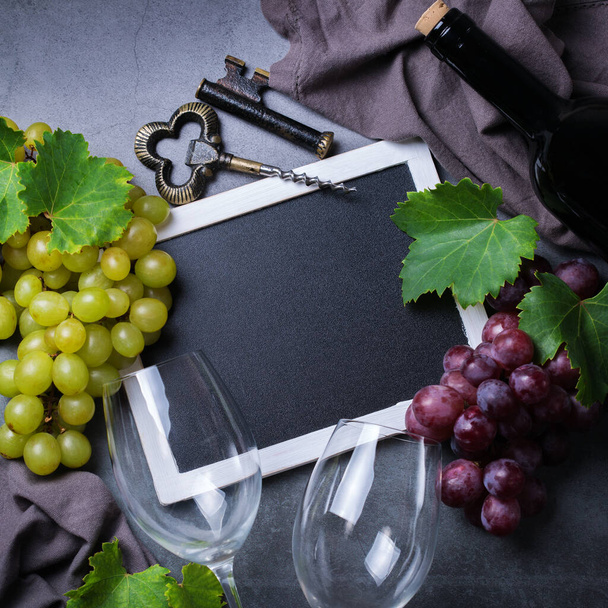 Eten en drinken, herfst herfst concept. Wijnproeverij, degustation, uitnodigingskaart met symbolen - wijnstok, fles, glazen, kurkentrekker. Kopieer ruimte zwarte achtergrond - Foto, afbeelding