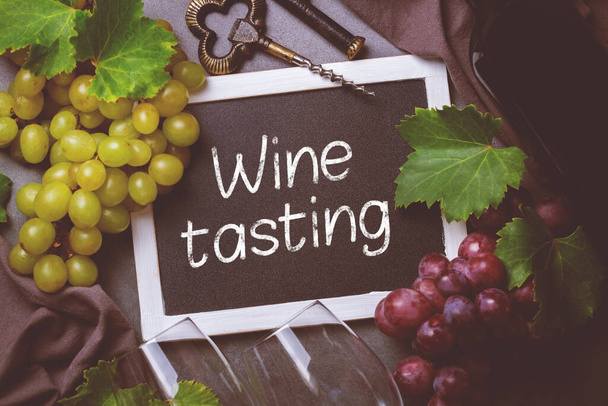 Food and drink, harvest autumn fall concept. Wine tasting, degustation, invitation card with symbols - grape vine, bottle, glasses, corkscrew. Black background, toned - Photo, Image