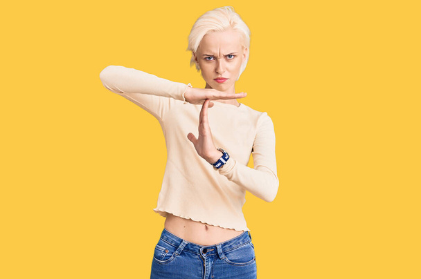 Młoda blondynka w luźnych ubraniach robi gest rękami, sfrustrowana i poważna twarz  - Zdjęcie, obraz